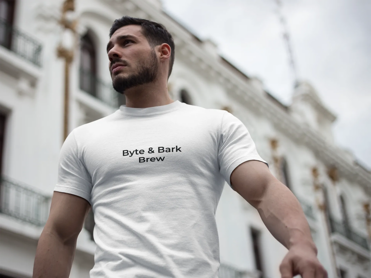 Low-angle portrait of man wearing white tee with Byte & Bark Brew® text, blurred building background