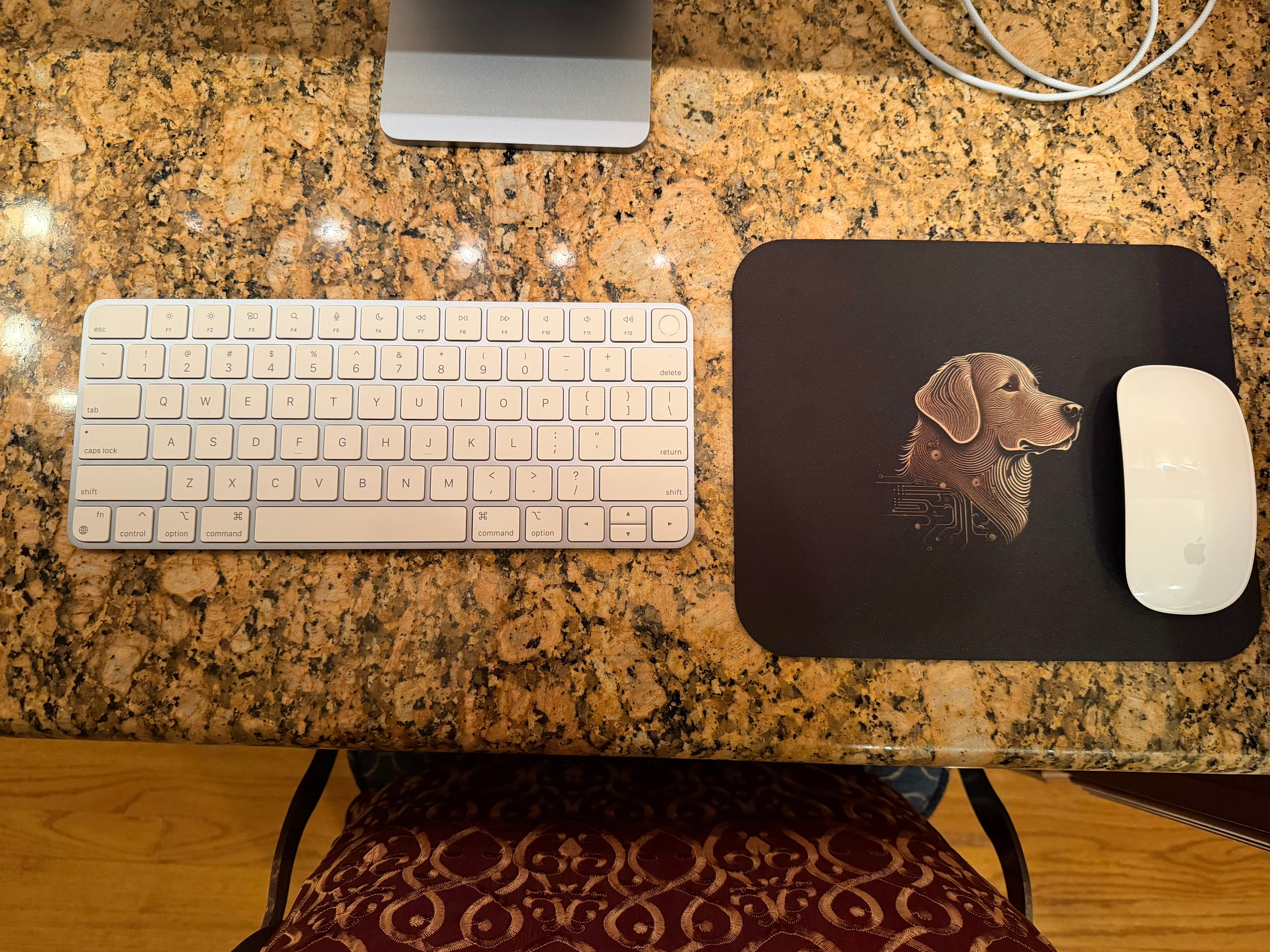 Keyboard, mouse, and mouse pad with a dog design on a granite countertop.
