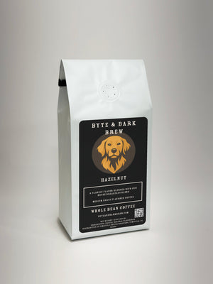 A white bag of Byte & Bark Brew Hazelnut whole bean coffee, featuring a black label with a golden retriever logo, set against a neutral light gray background.