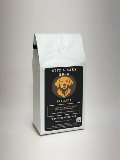 A white bag of Byte & Bark Brew Hazelnut whole bean coffee, featuring a black label with a golden retriever logo, set against a neutral light gray background.