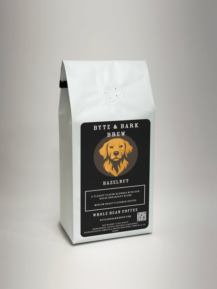 A white bag of Byte & Bark Brew Hazelnut whole bean coffee, featuring a black label with a golden retriever logo, set against a neutral light gray background.