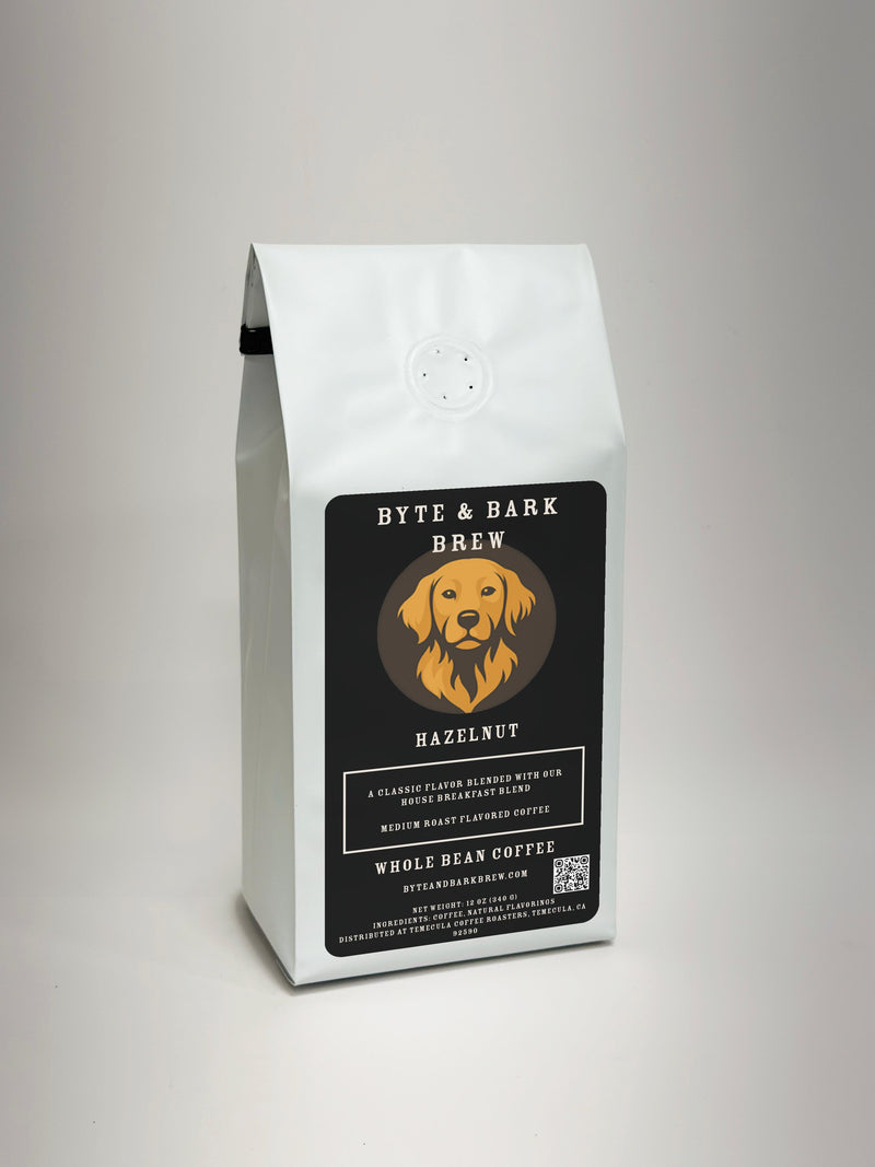 A white bag of Byte & Bark Brew Hazelnut whole bean coffee, featuring a black label with a golden retriever logo, set against a neutral light gray background.