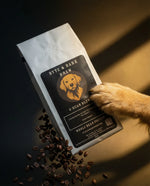 Dog paw touching a coffee bag labeled 'Byte & Dark Brew' with scattered coffee beans on a dark background.