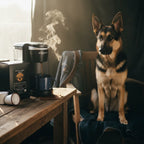 Dog sitting next to a Keurig coffee maker on a wooden table with steam rising.